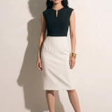 A professional woman modeling an elegant black and white color-block sheath dress, featuring a sleeveless black bodice with metallic hardware and a tailored white pencil skirt for a sophisticated executive look.