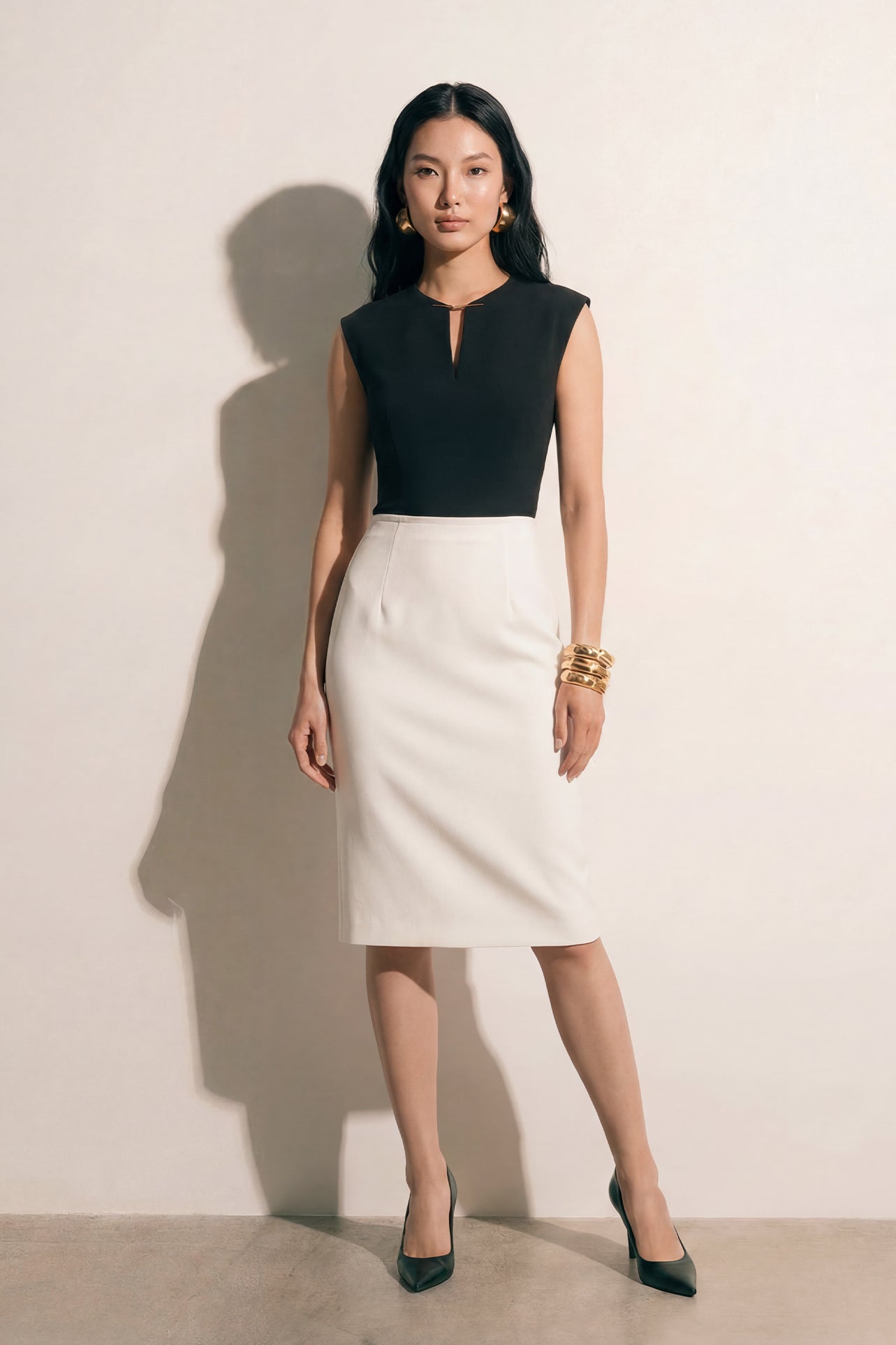 A professional woman modeling an elegant black and white color-block sheath dress, featuring a sleeveless black bodice with metallic hardware and a tailored white pencil skirt for a sophisticated executive look.
