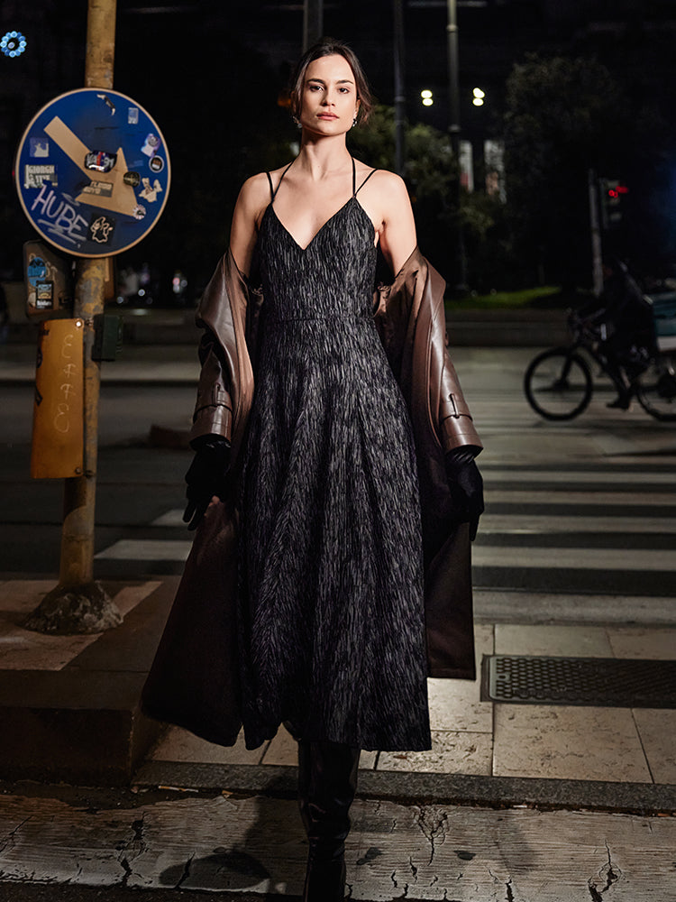 Fashionable black cami dress featuring a distinctive crinkled fabric and an expansive flared hem, paired with a brown coat, against an urban setting.