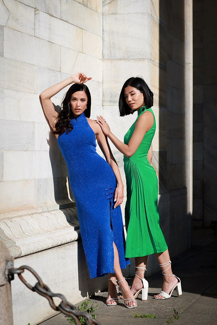 Two models against a wall, one in blue and the other in green off-shoulder knitted Cheongsam dresses, exemplifying the blend of traditional and modern fabric technology.