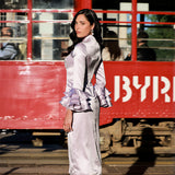 Model in a silk Cheongsam dress with a cityscape background featuring a red bus, blending traditional elegance with urban vibrancy.
