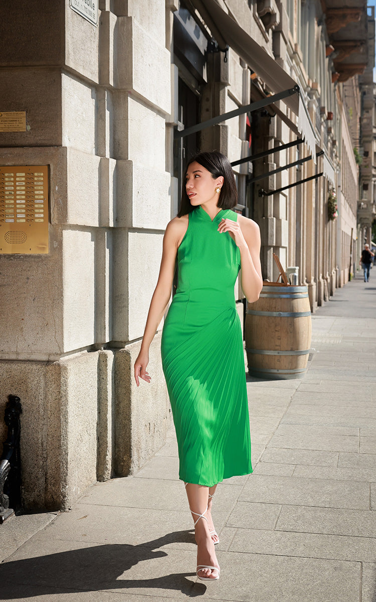 Model in SENSEBYMEI's Wang collection Cheongsam, in nature-inspired grass green, stands amidst the cityscape, showcasing the asymmetrical pleated design and modern shoulder cut.
