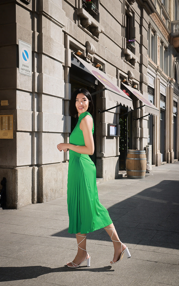 Side view of a model wearing a modern Chinese-inspired green Cheongsam dress with sun pleats and slant-cut design, set against an urban backdrop.