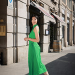 Side view of a model wearing a modern Chinese-inspired green Cheongsam dress with sun pleats and slant-cut design, set against an urban backdrop.