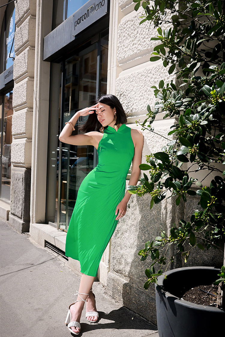 Model in a grass green Cheongsam from the Wang collection leans against a city wall, highlighting the dynamic silhouette and elegant minimalism of the dress.