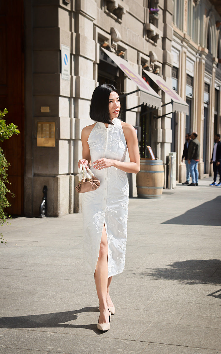 Model in a 3D Lace Flower Cheongsam Dress with a high-quality satin base, tilting her head to the side against an urban cityscape, showcasing the metallic sheen and embroidered details.