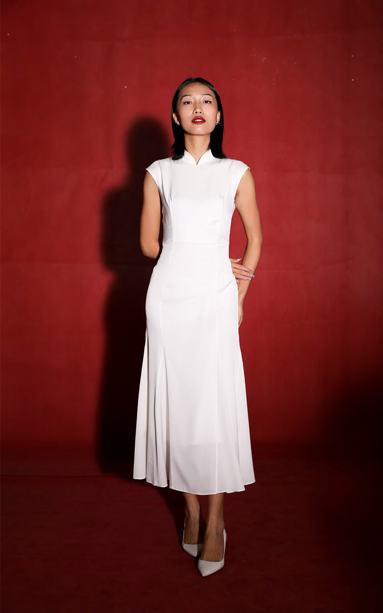 Frontal view of a model in Brand by Mei's white silk mermaid Cheongsam, set against a vibrant red backdrop, highlighting the blend of traditional elegance and modern design.