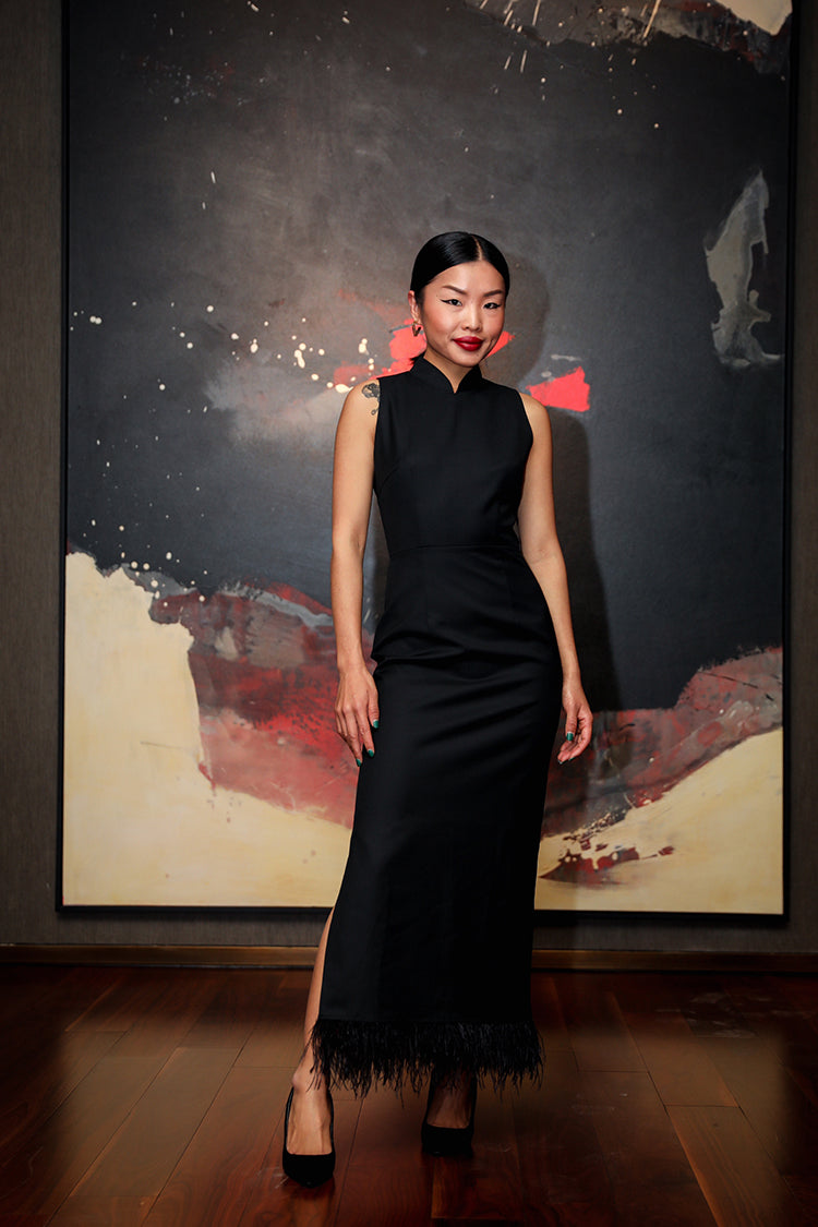 Model in a luxurious long black Cheongsam dress with ostrich feather spliced Mandarin collar, sourced from China's premier Yang* Group, posing in an elegant setting.