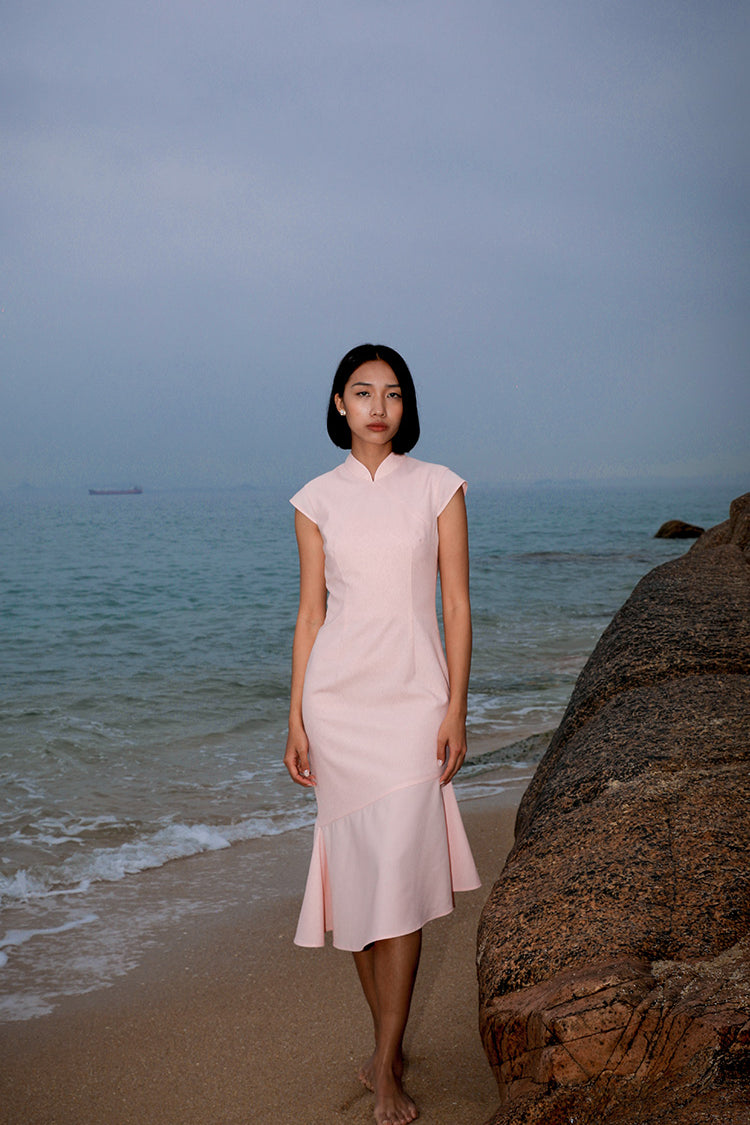 Model in a pure color modern Cheongsam mermaid dress in soft pink, elegantly posed by the seaside, showcasing the crescent moon motif and luxurious fine wool fabric.