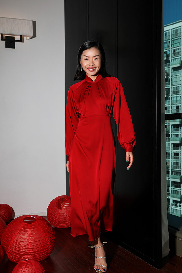 Smiling model in a pure red silk modern Cheongsam dress, enhancing her natural grace within a traditional Chinese setting.