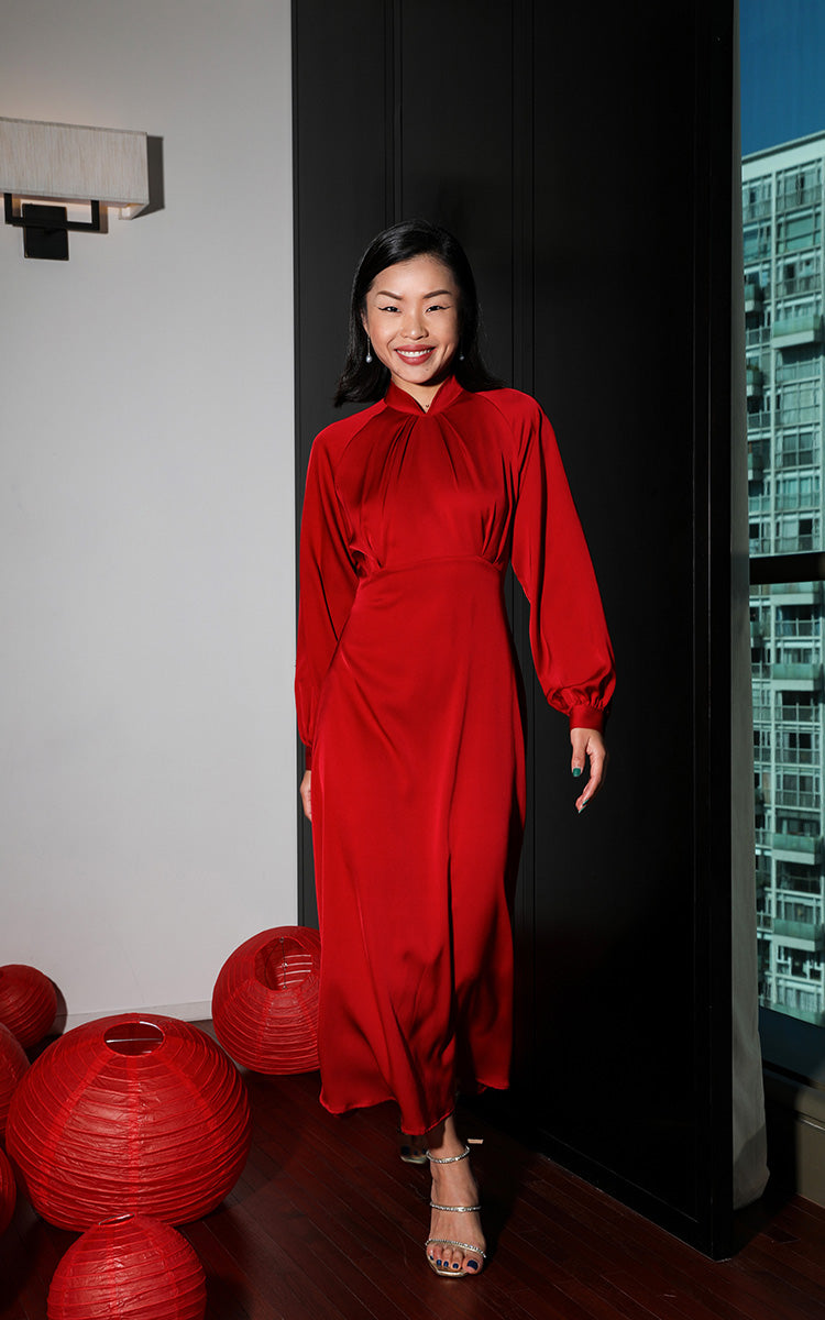 Smiling model in a pure red silk modern Cheongsam dress, enhancing her natural grace within a traditional Chinese setting.