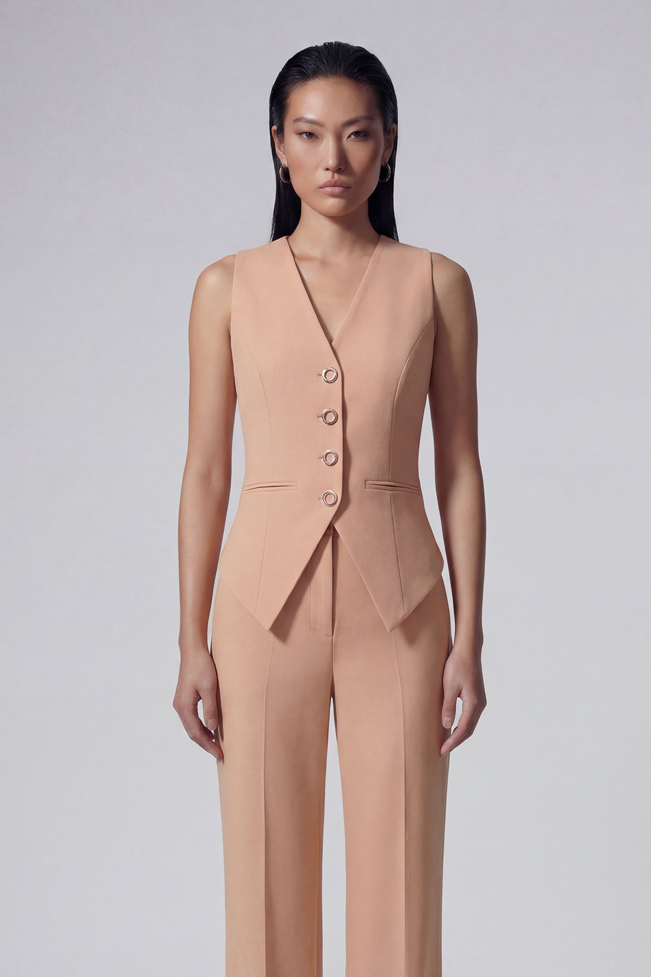 A professional woman wearing a sophisticated apricot-colored tailored vest, featuring a deep V-neckline and a unique pointed hem for an elegant executive office look.