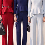 A style comparison of three women wearing tailored two-piece power suits featuring long-sleeve split V-neck jackets with dramatic asymmetrical peplum hems and matching cuffed wide-leg trousers; shown in vibrant crimson red, deep navy blue, and pale ice blue.