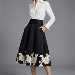 An elegant woman wearing a sophisticated black A-line midi dress, featuring exquisite white floral embroidery along the hem and professional three-quarter sleeves for a timeless formal look.