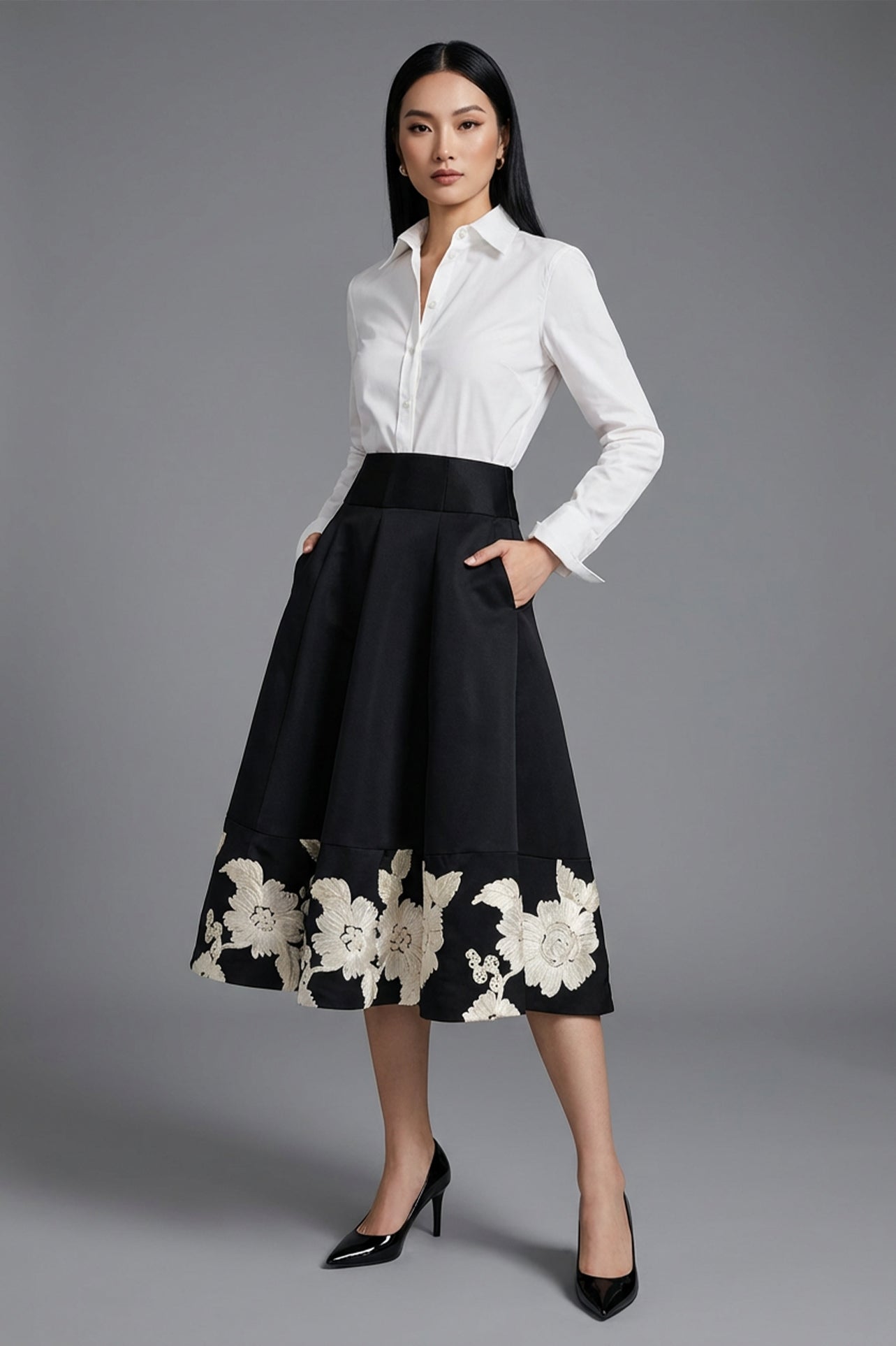 An elegant woman wearing a sophisticated black A-line midi dress, featuring exquisite white floral embroidery along the hem and professional three-quarter sleeves for a timeless formal look.