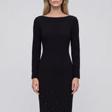 An elegant woman wearing a classic black long-sleeve sheath midi dress featuring a sophisticated boat neckline and a stunning gradient of sparkling rhinestones at the hemline for a refined evening look.