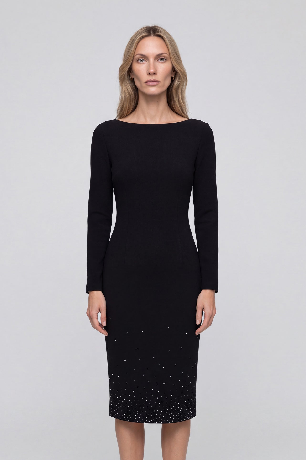 An elegant woman wearing a classic black long-sleeve sheath midi dress featuring a sophisticated boat neckline and a stunning gradient of sparkling rhinestones at the hemline for a refined evening look.
