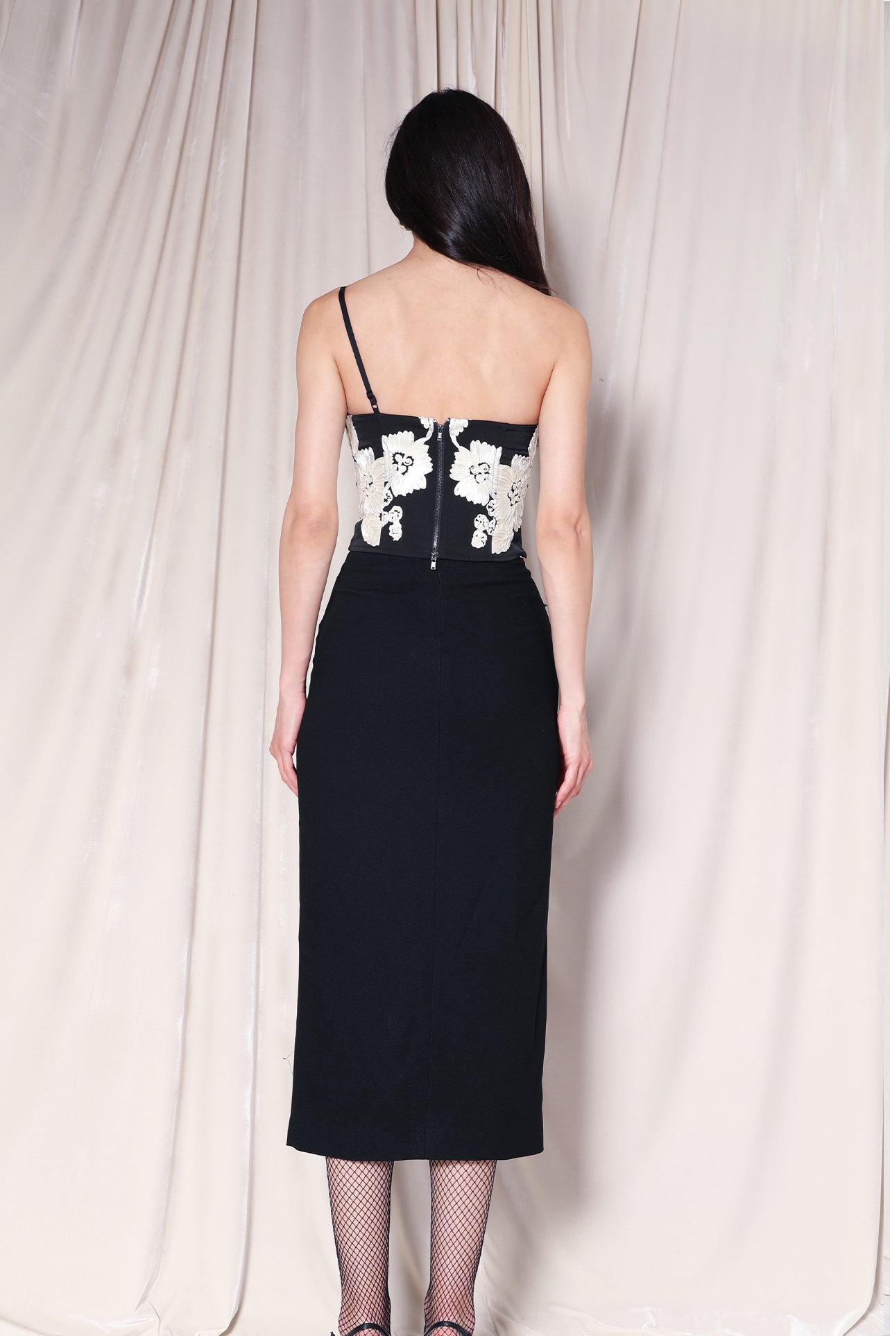 A professional woman wearing a sophisticated high-waisted black pencil skirt, featuring elegant gold-tone mandarin-style buttons and a stylish side slit for a polished executive office look.