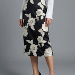 A professional woman wearing a sophisticated high-waisted black pencil skirt, intricately decorated with large white floral embroidery for a polished and elegant office or event look.