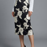 A professional woman wearing a sophisticated high-waisted black pencil skirt, intricately decorated with large white floral embroidery for a polished and elegant office or event look.