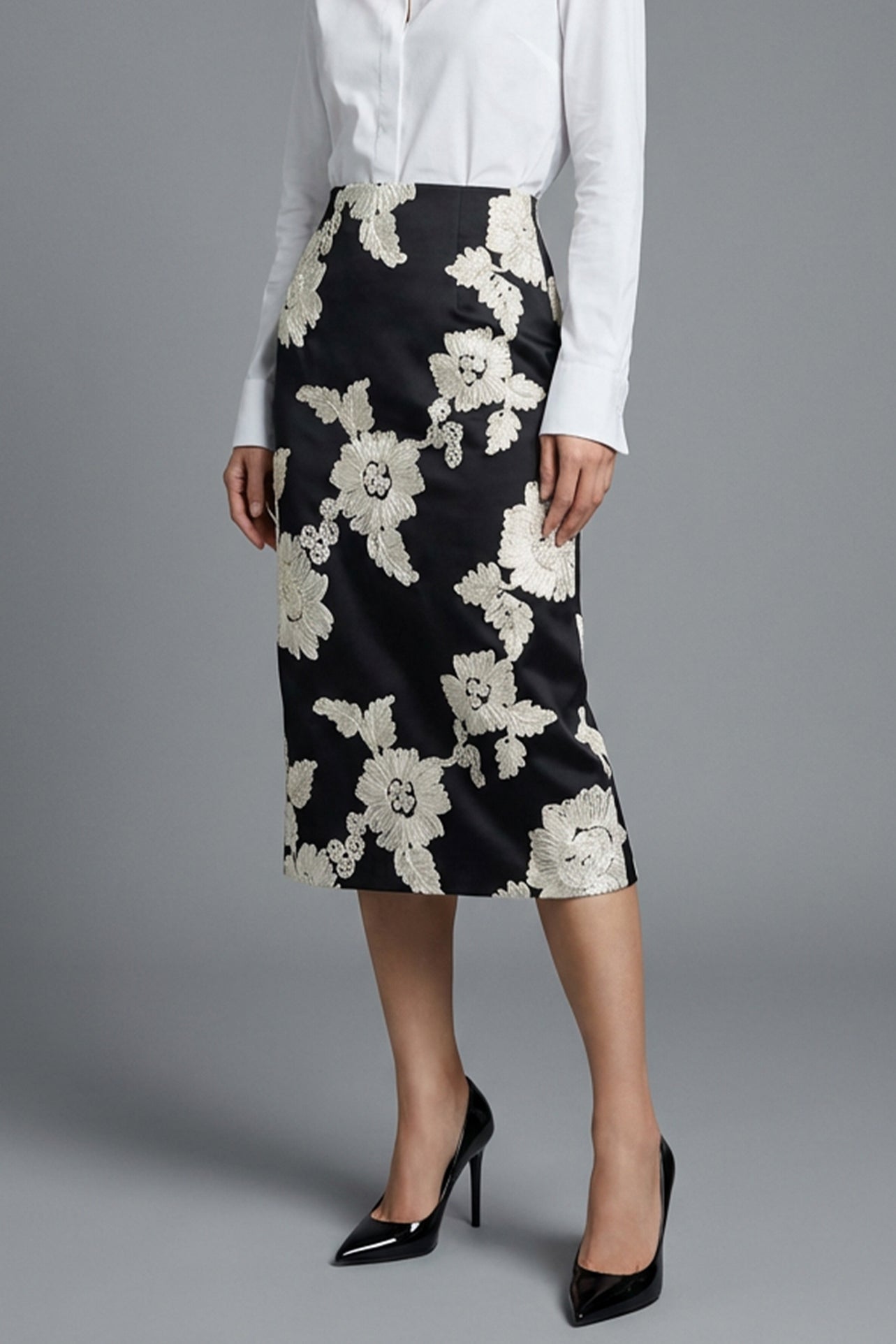 A professional woman wearing a sophisticated high-waisted black pencil skirt, intricately decorated with large white floral embroidery for a polished and elegant office or event look.