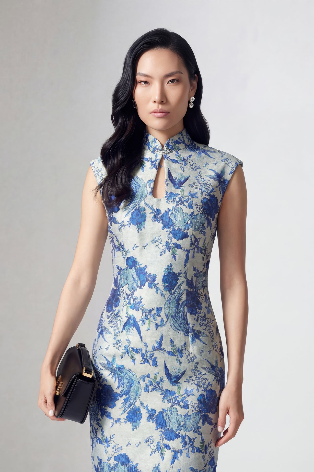 A professional woman wearing a sophisticated modern qipao dress, featuring a blue and white porcelain floral print, a mandarin collar with keyhole detail, and a slimming tailored fit for an elegant executive look.