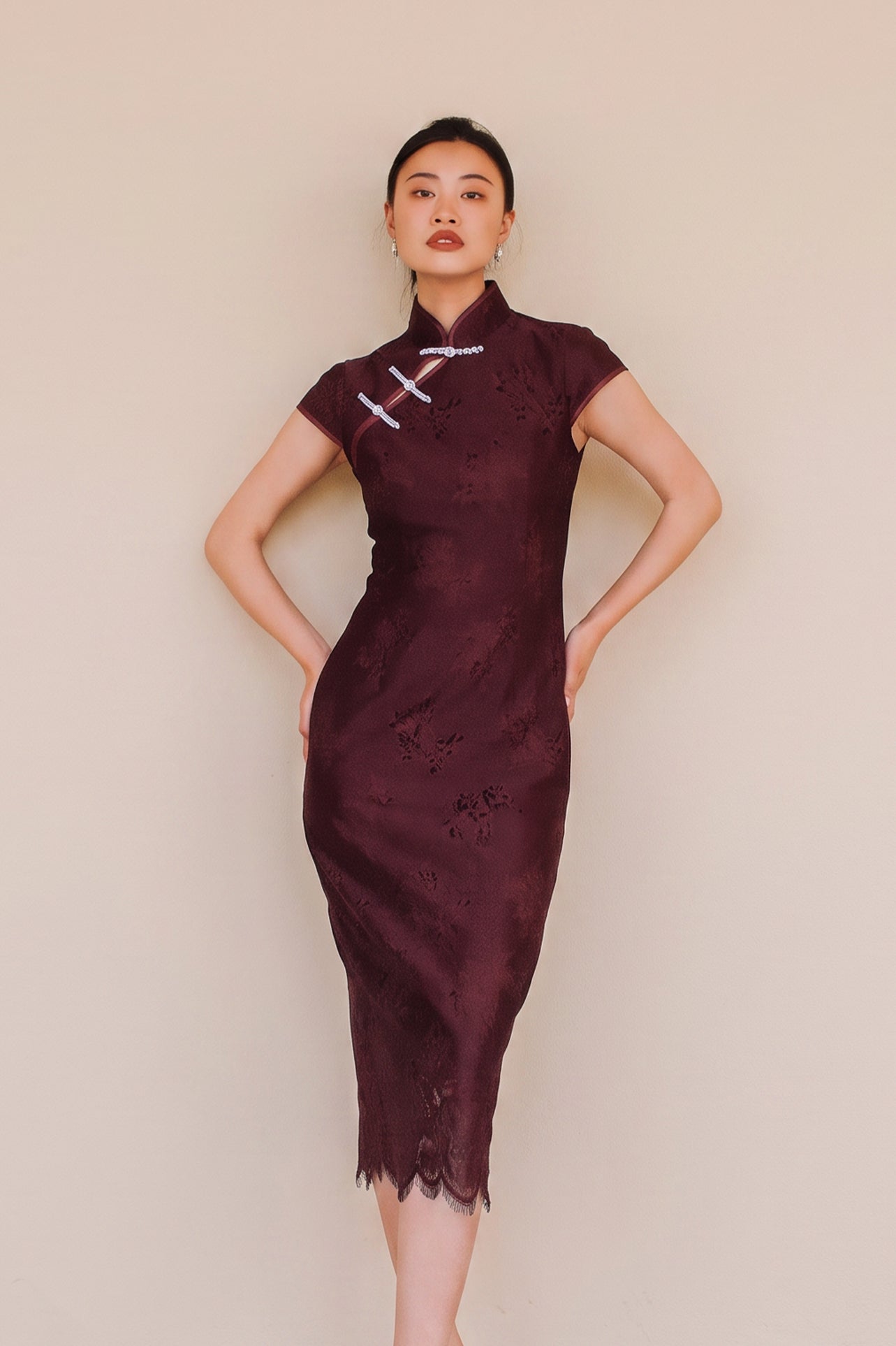 An elegant woman wearing a sophisticated burgundy jacquard modern qipao cheongsam dress featuring a classic mandarin collar, delicate contrast frog closures, cap sleeves, and a tailored sheath silhouette.