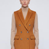 A chic professional woman wearing a tailored camel double-breasted longline suit vest featuring classic notch lapels and flap pockets, layered over a soft beige turtleneck sweater for a sophisticated quiet luxury look.