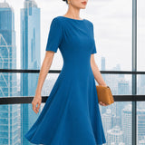 A beautiful model wearing a sophisticated medium blue A-line midi dress featuring an elegant boat neckline with refined asymmetric shoulder pleating, short sleeves, and a flowing flared swing skirt.