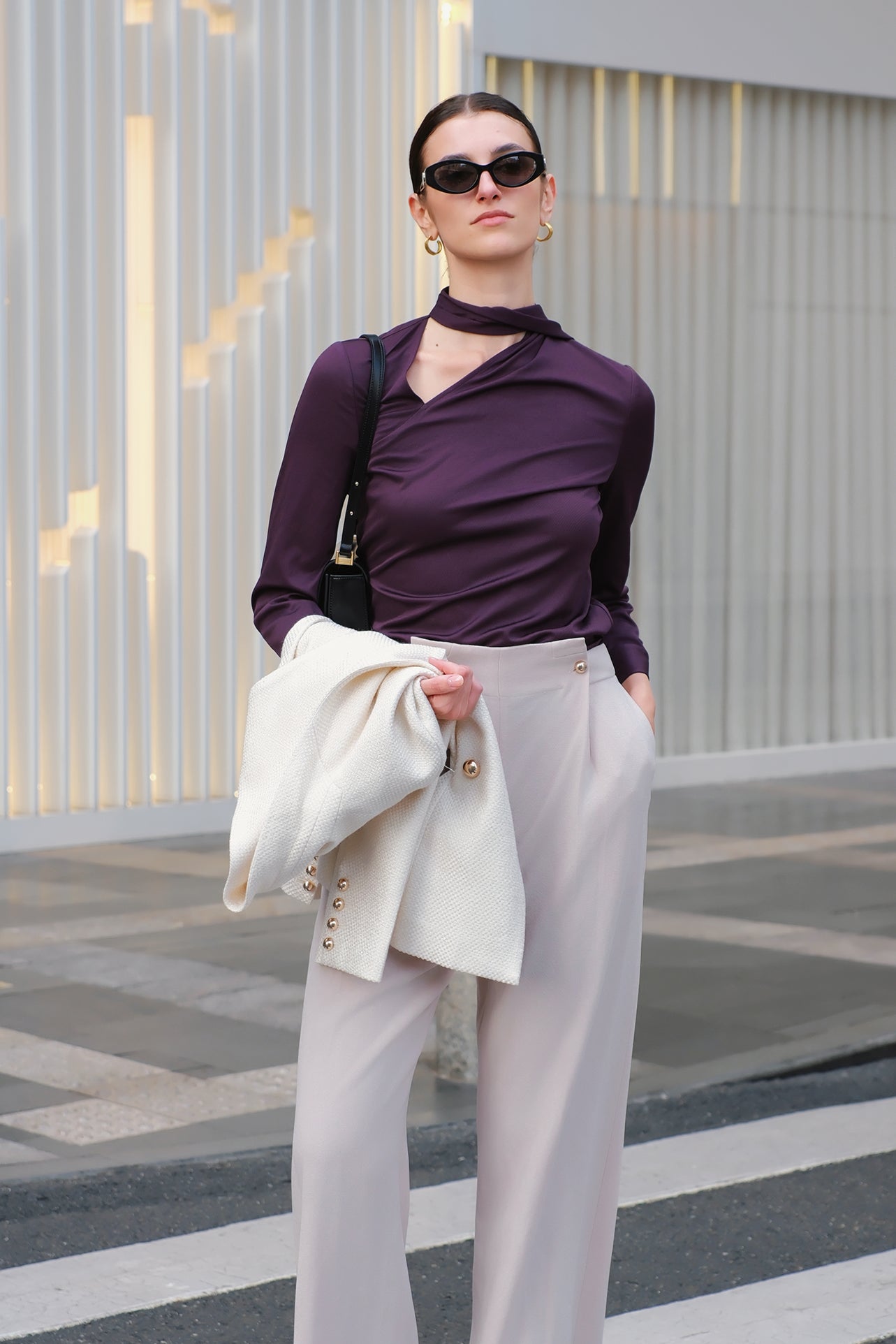 A chic woman wearing an elegant deep plum long-sleeve blouse with an asymmetric high-neck scarf tie, neatly tucked into a high-waisted black tweed skirt embellished with subtle sparkling sequins.