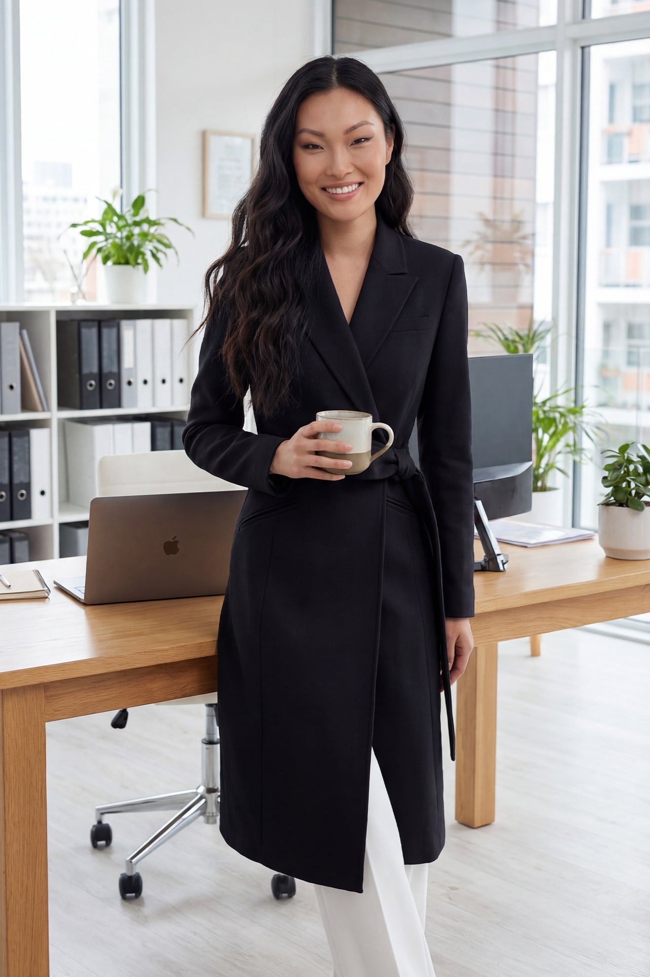 A professional woman wearing a sophisticated black long-sleeve coat dress, featuring an elegant tie-waist belt and notched lapels, styled over a white shirt for a polished executive business look.