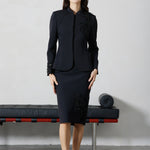 A professional woman wearing a sophisticated black skirt suit, featuring a mandarin collar with elegant leaf embroidery on the shoulder and skirt, and traditional frog button detailing for a modern oriental executive look.