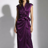A professional woman modeling an elegant deep purple satin wrap midi dress, featuring a sophisticated surplice V-neck, cap sleeves, and a chic side bow tie for a quiet luxury evening or office look.