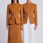 A chic professional Asian woman wearing a luxurious camel wool tailored jacket featuring a sleek stand collar, exposed two-way front zipper, structured shoulders, and an hourglass silhouette paired with a matching skirt.