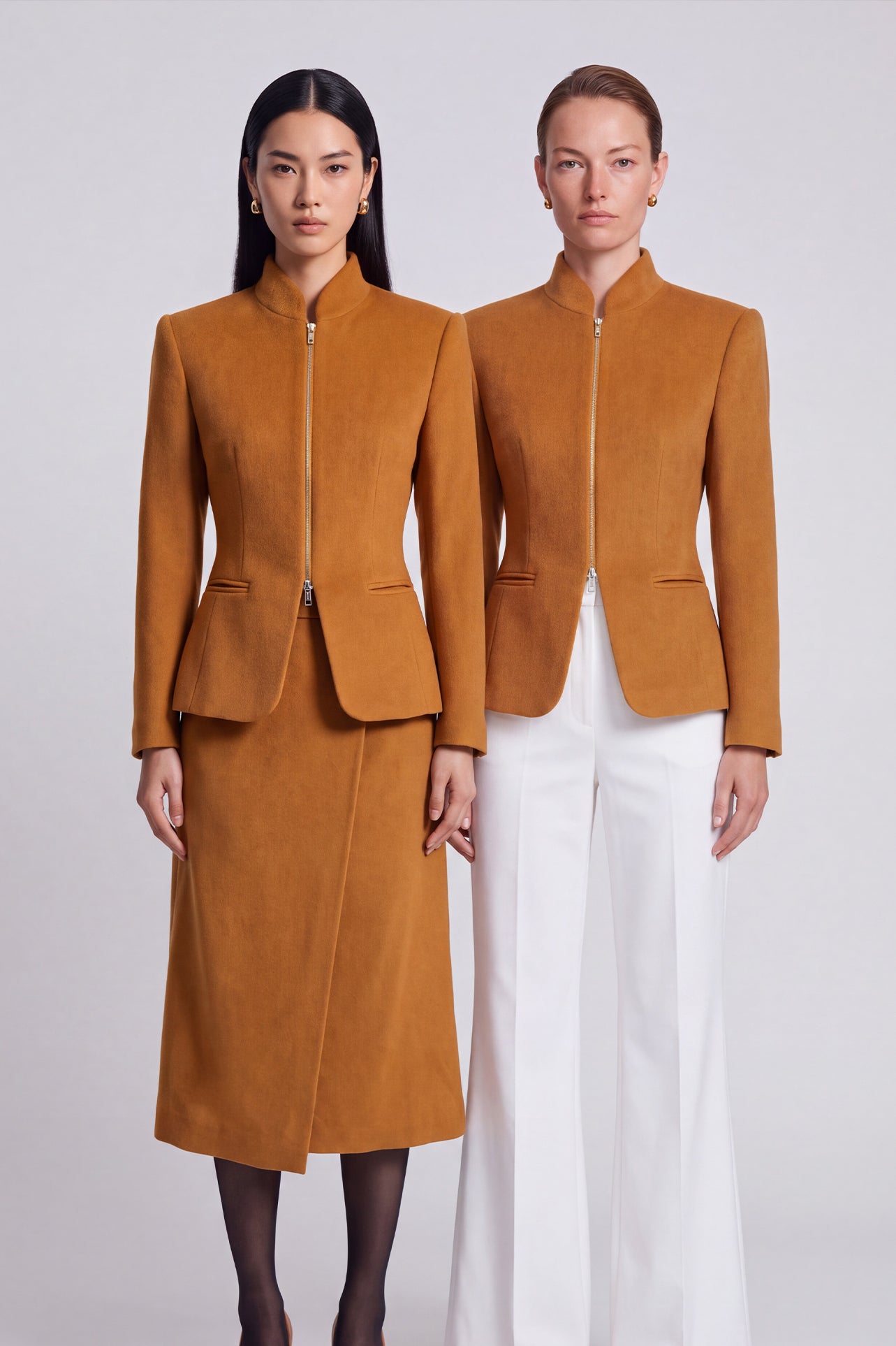 A chic professional Asian woman wearing a luxurious camel wool tailored jacket featuring a sleek stand collar, exposed two-way front zipper, structured shoulders, and an hourglass silhouette paired with a matching skirt.
