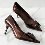 A pair of elegant dark chocolate brown patent leather pumps featuring a pointed toe and a sophisticated 3D rose floral decoration on the front, perfect for a quiet luxury office or evening look.
