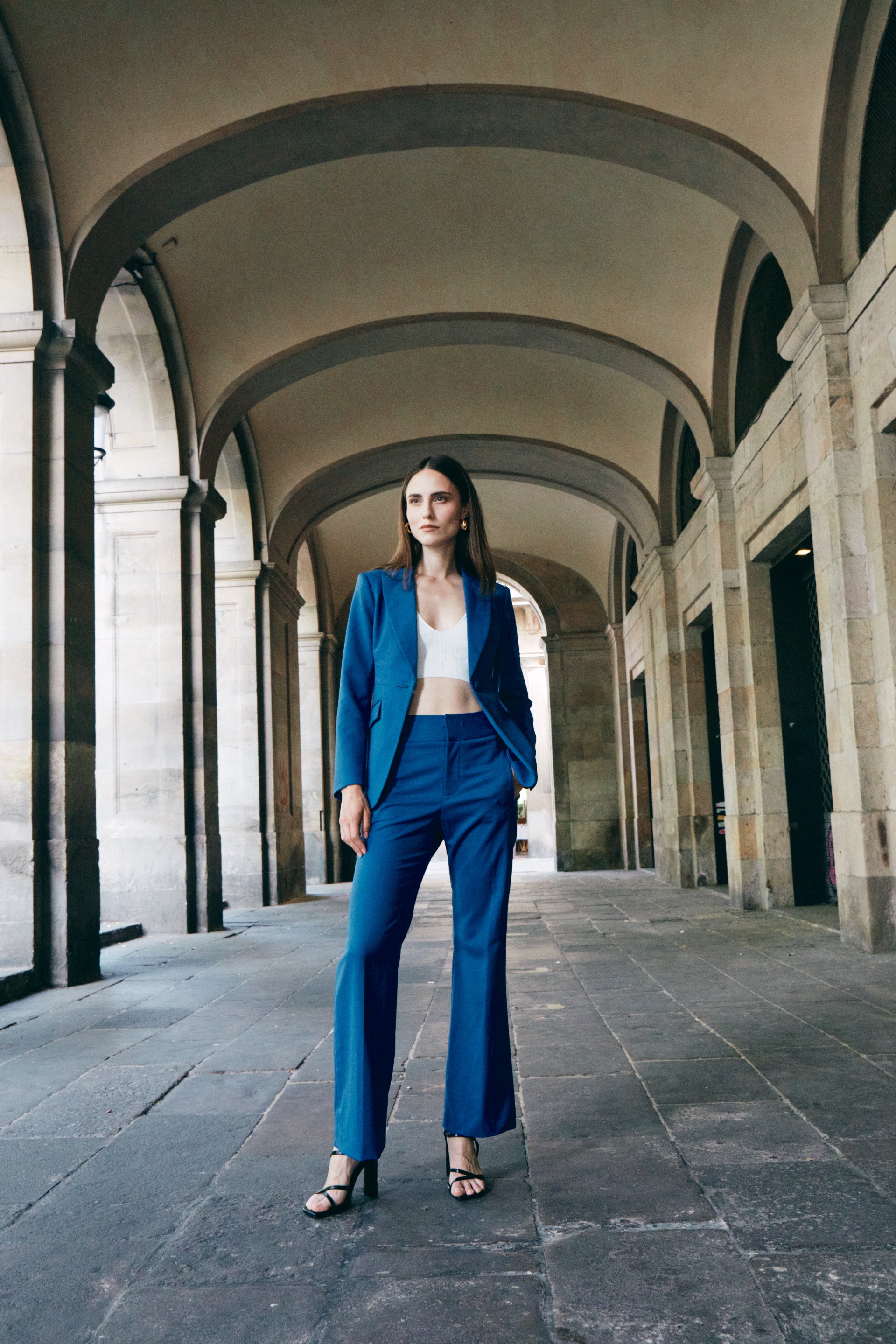 A professional woman wearing sophisticated royal blue high-waisted wide-leg trousers, featuring a tailored loose-fit silhouette for a modern and vibrant executive office look.