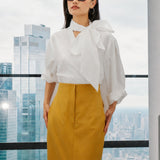 A style collection of three models presenting elegant dopamine office wear; the left in a white bow-tie blouse with a mustard yellow front-slit midi skirt, the center wearing a blue striped pussy-bow shirt with a straw hat and white wide-leg trousers, and the right in a vibrant orange satin blouse with a royal blue pencil skirt.