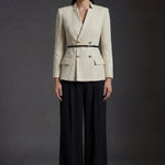 A professional woman wearing a sophisticated cream white tweed skirt suit, featuring a double-breasted blazer with gold buttons, a slim black belt, and an elegant polka dot pussy bow tie for a polished French chic office look.