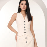A professional woman wearing a sophisticated off-white pinstripe vest top, featuring a slim-fit tailored silhouette, classic V-neck, and contrasting black buttons for a modern business casual look.