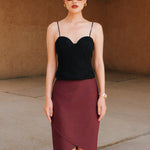 A style comparison of two elegant women's high-waisted pencil skirts featuring an overlapping crossover tulip hemline; shown on the left in deep navy blue paired with a white shirt, and on the right in rich burgundy wine paired with a matching long-sleeve top and suede clutch.