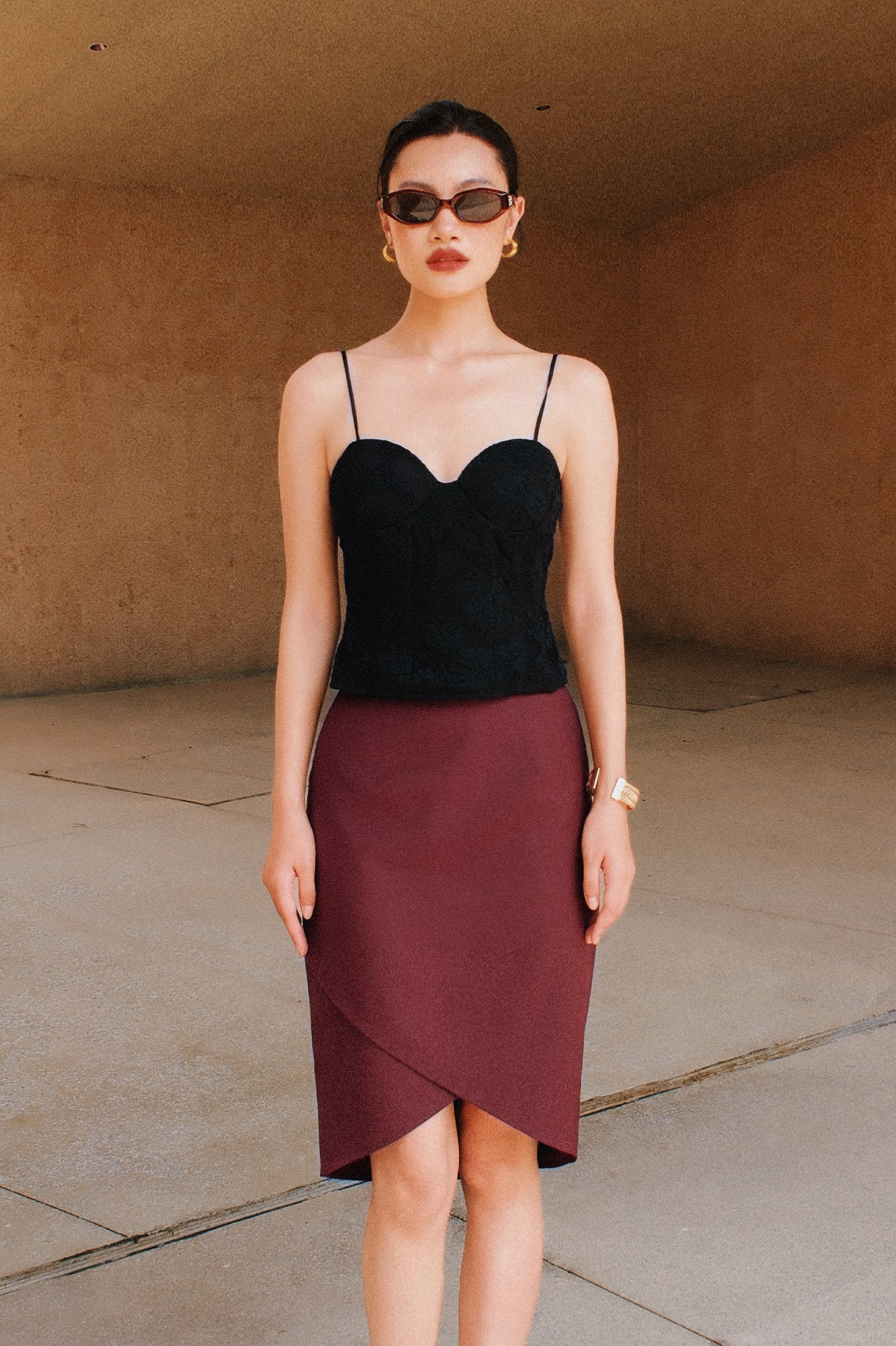 A style comparison of two elegant women's high-waisted pencil skirts featuring an overlapping crossover tulip hemline; shown on the left in deep navy blue paired with a white shirt, and on the right in rich burgundy wine paired with a matching long-sleeve top and suede clutch.