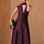 A chic woman wearing sunglasses and an elegant deep burgundy sleeveless V-neck A-line midi dress featuring textured jacquard fabric, delicate lace hemline, and a matching flowing neck scarf.