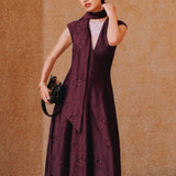 A chic woman wearing sunglasses and an elegant deep burgundy sleeveless V-neck A-line midi dress featuring textured jacquard fabric, delicate lace hemline, and a matching flowing neck scarf.