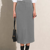 A stylish woman wearing a sophisticated grey pinstripe high-waisted midi skirt with a front slit, paired with a white button-up shirt rolled at the sleeves and black ankle boots for a minimalist corporate chic look.