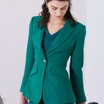 A professional woman wearing a sophisticated emerald green tailored blazer, featuring a slim-fit silhouette, notched lapels, and flap pockets, styled elegantly with a patterned silk scarf for a corporate office look.