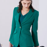 A professional woman wearing a sophisticated emerald green tailored blazer, featuring a slim-fit silhouette, notched lapels, and flap pockets, styled elegantly with a patterned silk scarf for a corporate office look.