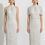 A professional woman modeling an elegant white lace halter neck modern qipao dress, featuring a sophisticated mandarin collar with keyhole detail and an intricate eyelet embroidered fabric for a quiet luxury look.