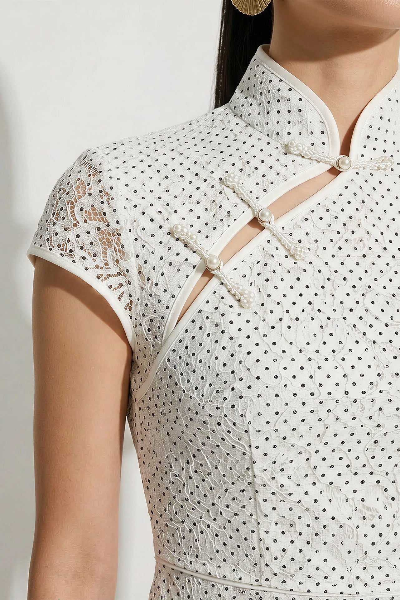 A professional woman modeling an elegant white lace modern qipao dress, featuring an intricate eyelet textured fabric, a sophisticated mandarin collar with a traditional knot button, and slimming cap sleeves.