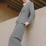 A beautiful professional model wearing an elegant grey pinstripe collarless blazer featuring a distinctive tie-front knot at the waist, styled with a crisp white collared shirt underneath for a modern corporate chic look.